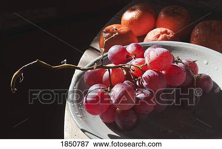 Stock Photo - Fruit; Red grapes on plate with mandarins in background . Fotosearch