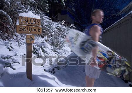 Stock Photo - Man holding a wakeboard; Wakeboarder in shorts in the snow. Fotosearch