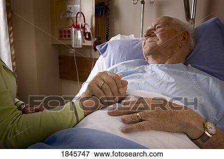 Man in a hospital bed; Man's hand being held by a woman View Large Photo Image Stock Photo - Man in a hospital bed; Man's hand being held by a woman. Fotosearch