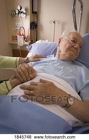 Stock Photo - Man in a hospital bed; Man's hand being held by a woman. Fotosearch