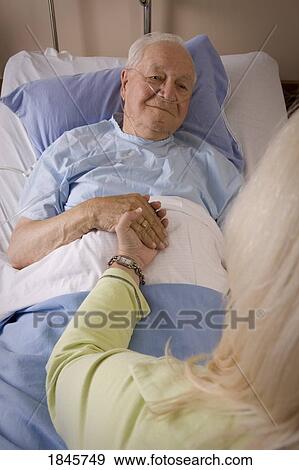 Man in a hospital bed; Man's hand being held by a woman View Large Photo Image Stock Photo - Man in a hospital bed; Man's hand being held by a woman. Fotosearch