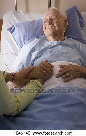 Man in a hospital bed; Man's hand being held by a woman View Large Photo Image Stock Photograph - Man in a hospital bed; Man's hand being held by a woman. Fotosearch