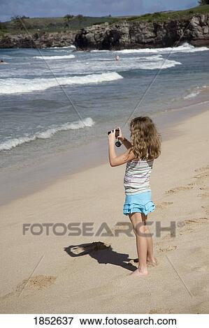 Stock Photo - Maui, Hawaii, USA; Girl taking a picture on the beach. Fotosearch