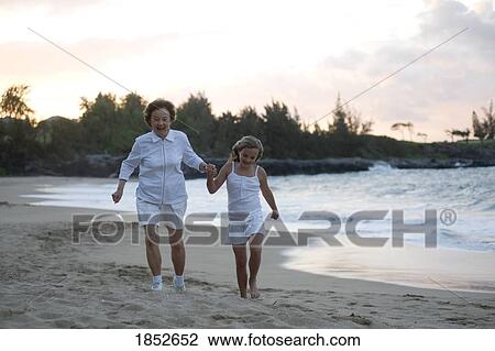 Stock Image - Maui, Hawaii, USA; Grandmother and granddaughter walking on the beach . Fotosearch