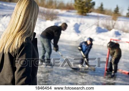 Picture - Mother watching father and sons play hockey. Fotosearch
