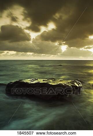 Stock Photo - Rock in shallow water under stormy sky. Fotosearch