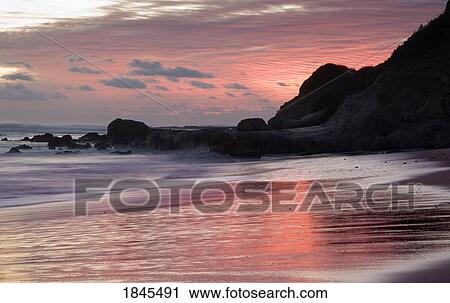 Stock Image - Sunset over water at a rocky shoreline. Fotosearch