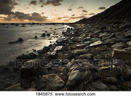 Sunset over water at a rocky shoreline View Large Photo Image Stock Photography - Sunset over water at a rocky shoreline. Fotosearch