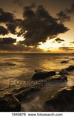 Sunset through dark clouds over water at a rocky shoreline View Large Photo Image Stock Photograph - Sunset through dark clouds over water at a rocky shoreline. Fotosearch