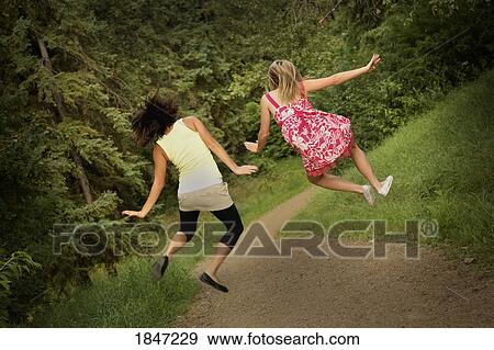 Stock Photo - Two teenage girls jumping in park. Fotosearch
