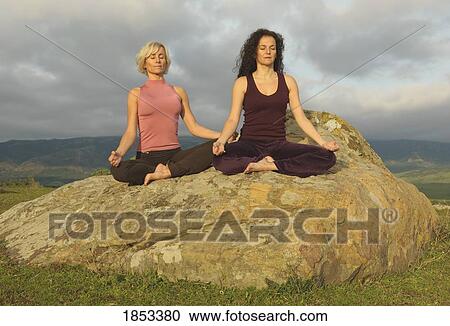 Stock Image - Two women on large boulder in yoga pose. Fotosearch