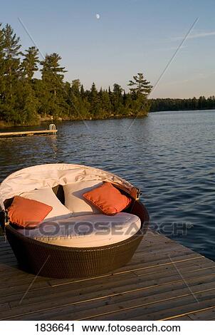 Stock Image - Wicker chair on dock, Lake of the Woods, Ontario, Canada. Fotosearch