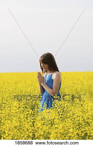 Stock Photo - A young woman praying in a canola field. Fotosearch