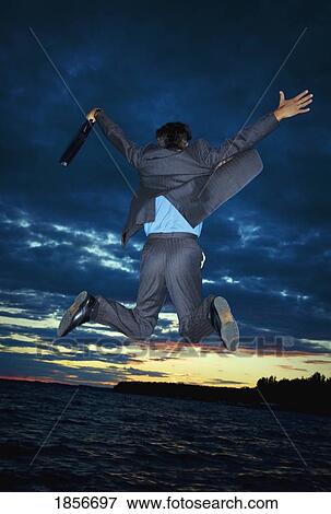 Stock Photo - Businessman jumping for joy before sunset scene. Fotosearch