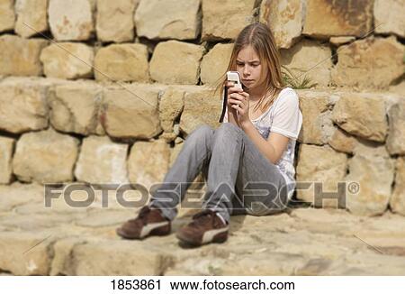 Girl texting on phone and sitting along stone wall View Large Photo Image Stock Image - Girl texting on phone and sitting along stone wall. Fotosearch