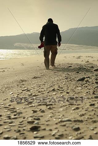 Man walking on a rocky beach View Large Photo Image Stock Photo - Man walking on a rocky beach. Fotosearch