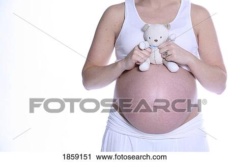 Stock Image - Pregnant woman holding teddy bear over bare belly. Fotosearch