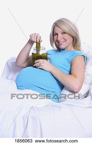 Stock Image - Pregnant woman in bed with a jar of pickles. Fotosearch