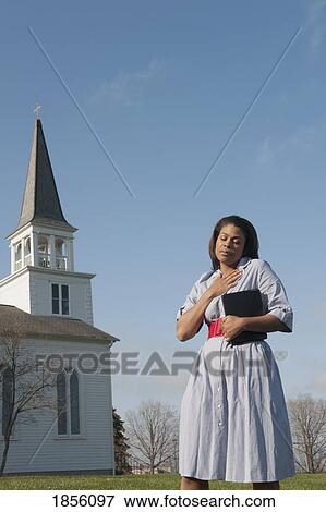 Stock Photo - Woman holding Bible and praying near a church. Fotosearch