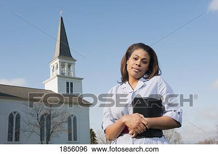 Woman holding Bible, standing near a church View Large Photo Image Stock Photograph - Woman holding Bible, standing near a church. Fotosearch