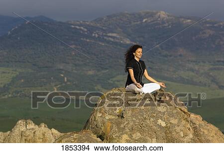 Picture - Woman in yoga pose on mountain top boulder. Fotosearch