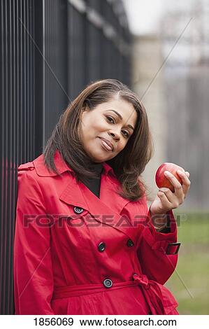 Stock Photo - Woman leaning against wrought iron fence, holding an apple. Fotosearch