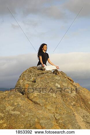 Stock Image - Woman meditating on a boulder. Fotosearch