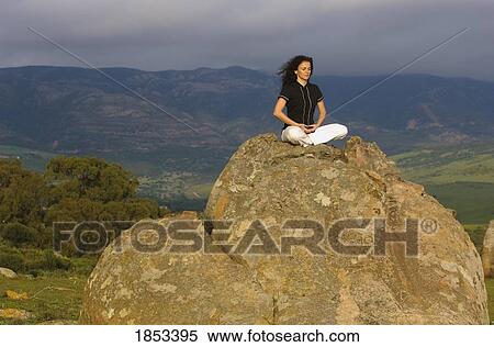 Stock Photography - Woman meditating on a boulder. Fotosearch