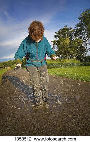 Stock Image - Woman playing in the rain puddles. Fotosearch