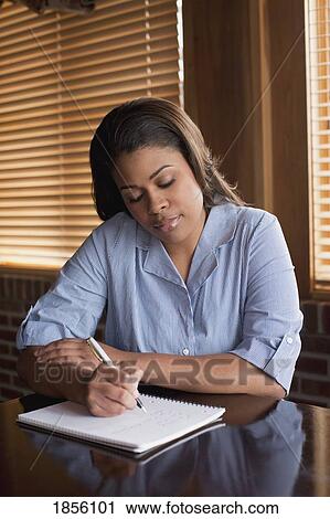 Stock Image - Woman sitting and writing on a pad of paper. Fotosearch