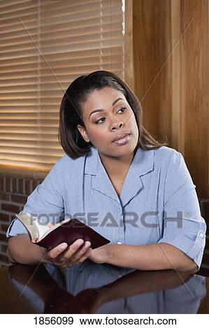 Stock Photo - Woman sitting at a table with Bible. Fotosearch