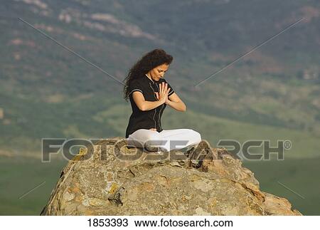 Stock Image - Woman sitting on mountain peak. Fotosearch