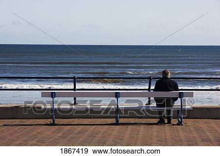 Stock Photo - Man sitting on seaside bench, Berwick, Northumberland, England. Fotosearch