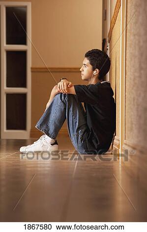 Stock Image - Teenage boy sitting on the floor listening to music. Fotosearch