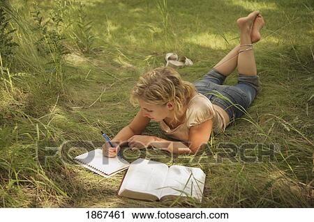 Stock Image - Woman laying in the grass and studying. Fotosearch