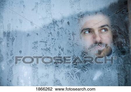 Stock Image - Young man looking out a frosted window. Fotosearch