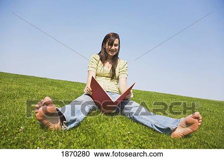Stock Image - a girl reading while sitting on the grass. Fotosearch