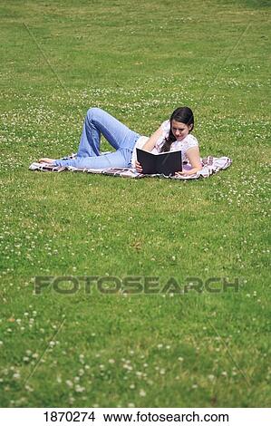 Picture - a teenage girl reading a book on a blanket on the grass. Fotosearch