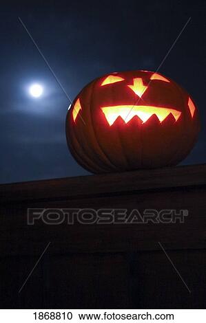 Stock Image - an illuminated jack-o-lantern on the fence at night. Fotosearch