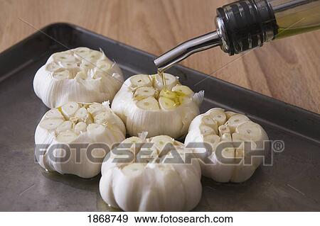 Stock Photo - bulbs of raw garlic on a baking sheet with olive oil poured on top. Fotosearch