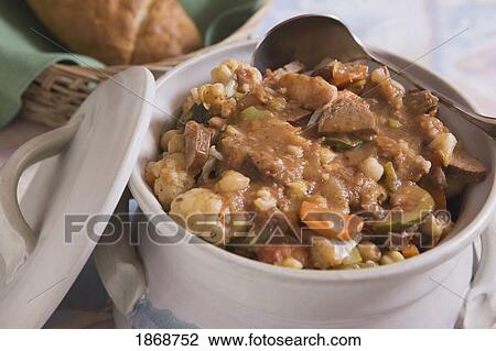 Stock Image - ceramic pot of beef stew and bread in a basket. Fotosearch
