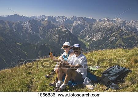 Stock Photograph - Couple sitting on a mountain top eating. Fotosearch