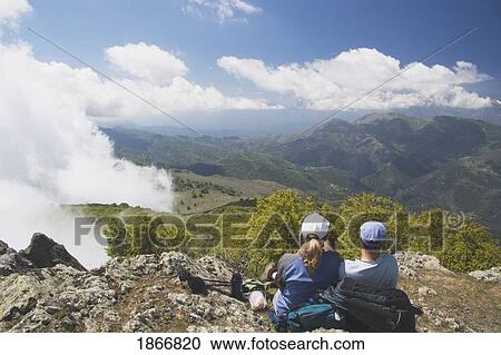 Stock Image - Couple sitting on the top of a mountain enjoying the view. Fotosearch