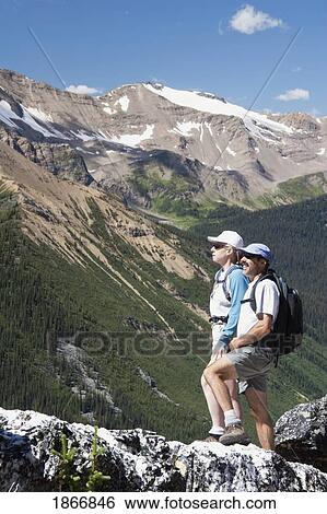 Stock Photograph - Couple standing on the top of a mountain. Fotosearch