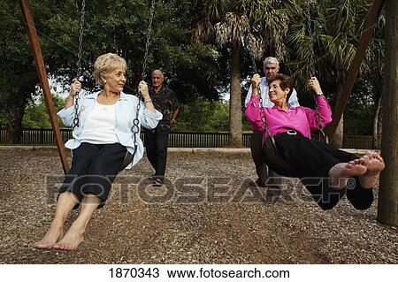 Stock Image - fort lauderdale, florida, united states of america; two married couples with the men pushing the women on the swings. Fotosearch