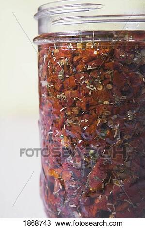 Stock Image - glass jar filled with sun dried tomatoes in herbs and oil. Fotosearch