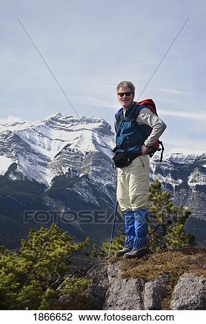 Stock Image - Hiker standing on a ledge in the mountains. Fotosearch