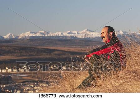 Man sitting and looking at the mountains View Large Photo Image Stock Photo - Man sitting and looking at the mountains. Fotosearch