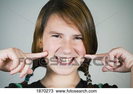 Stock Image - portrait of a girl pointing to her cheeks and smiling. Fotosearch