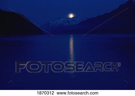 Stock Image - taiya inlet, skagway, alaska, united states of america; a moon over the chilkat mountains in the lynn canal of the inside passage. Fotosearch
